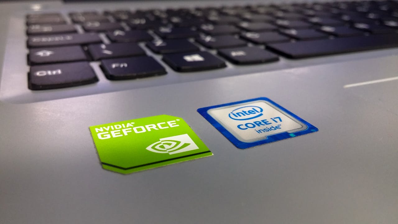 Auf dem Foto sind ein NVIDIA GeForce Aufkleber und ein Intel Core i7 Aufkleber auf einem Laptop zu sehen. Im Hintergrund sind auch einige Laptop-Tasten erkennbar